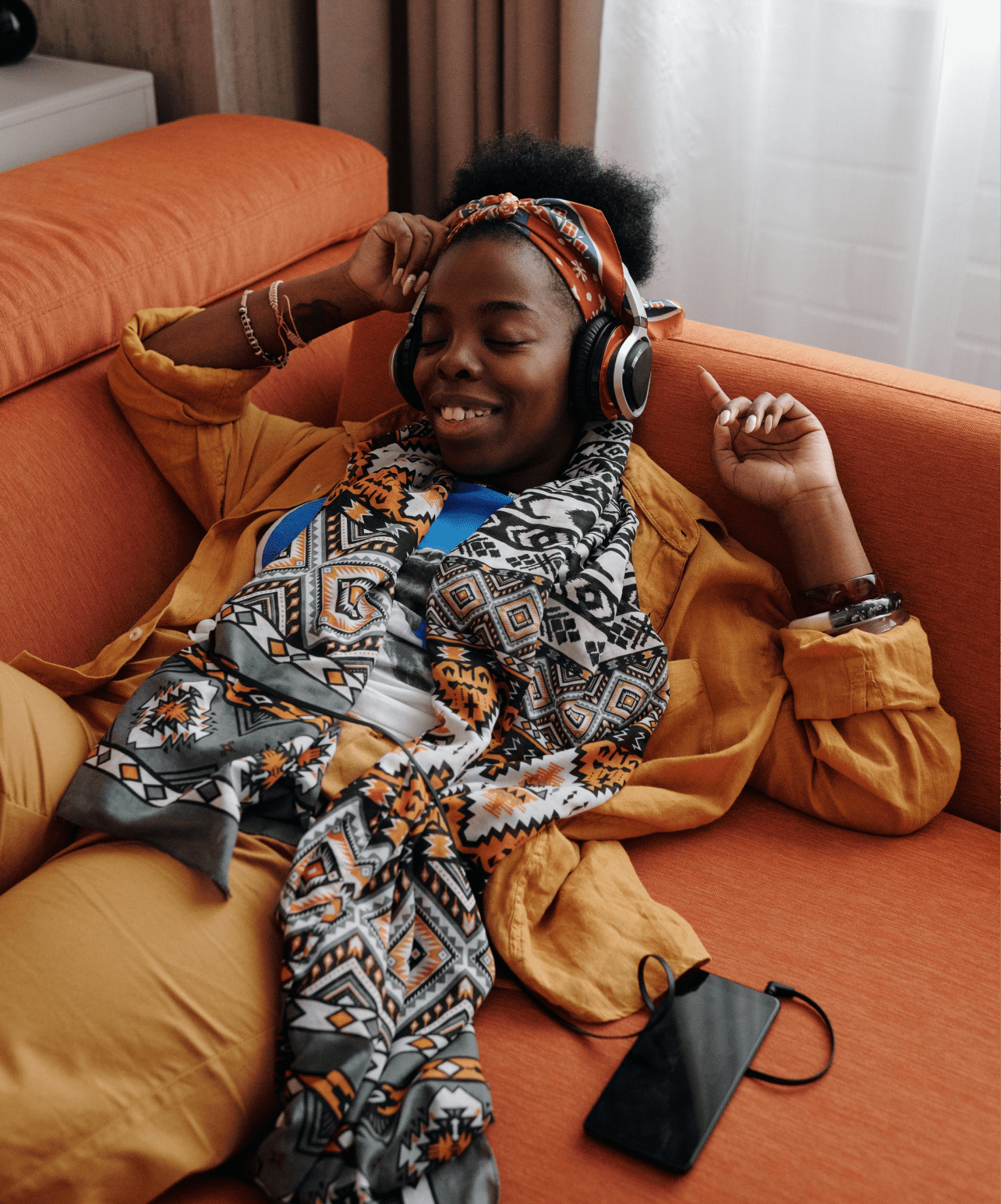 Woman lying on couch smiling while listening to podcast with headphones on