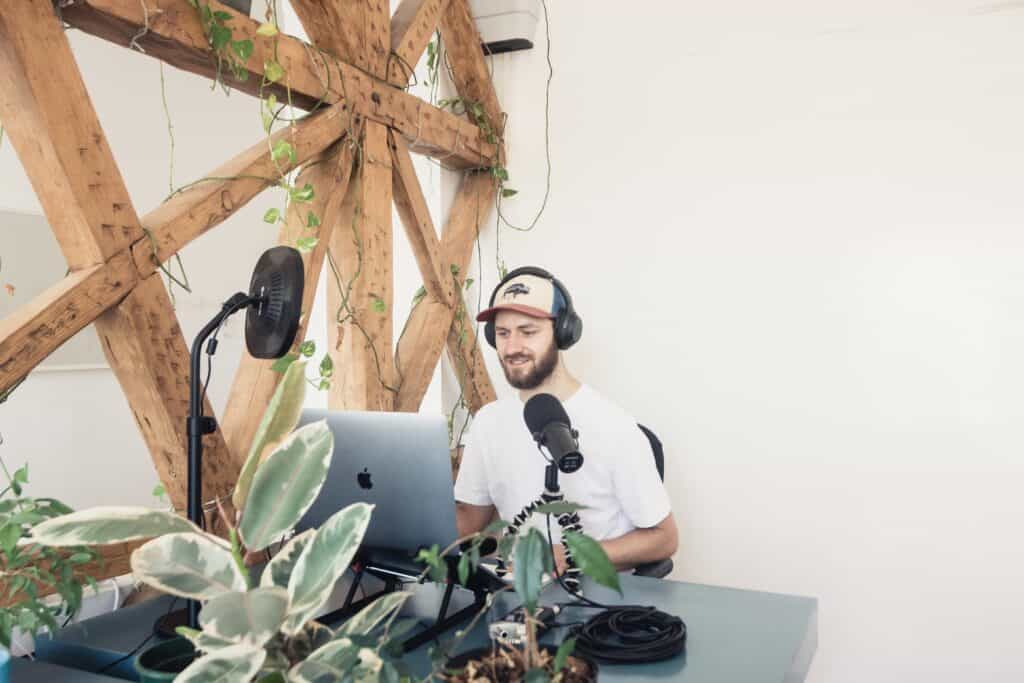 Man podcaster sitting at desk speaking into microphone with plants around him