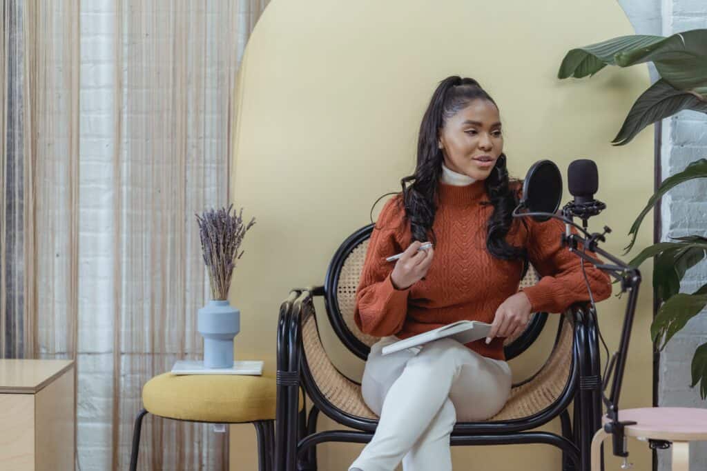 Woman podcaster sitting on chair speaking into microphone
