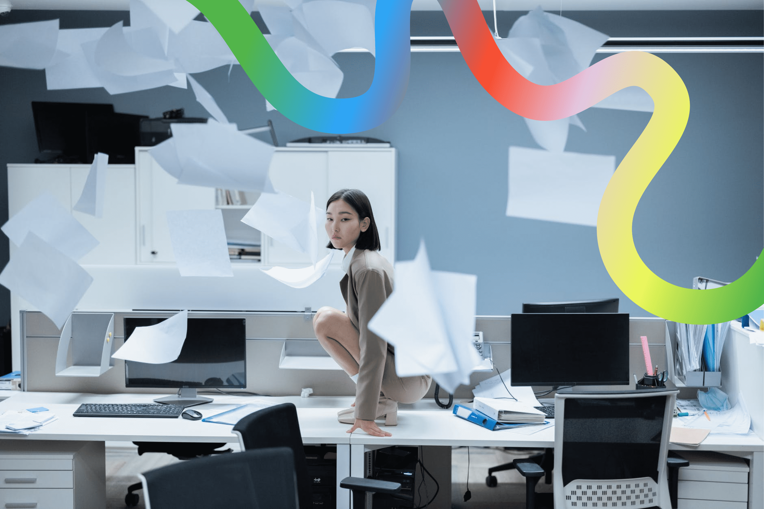 Woman squatting at her office desk with papers thrown in the air around her
