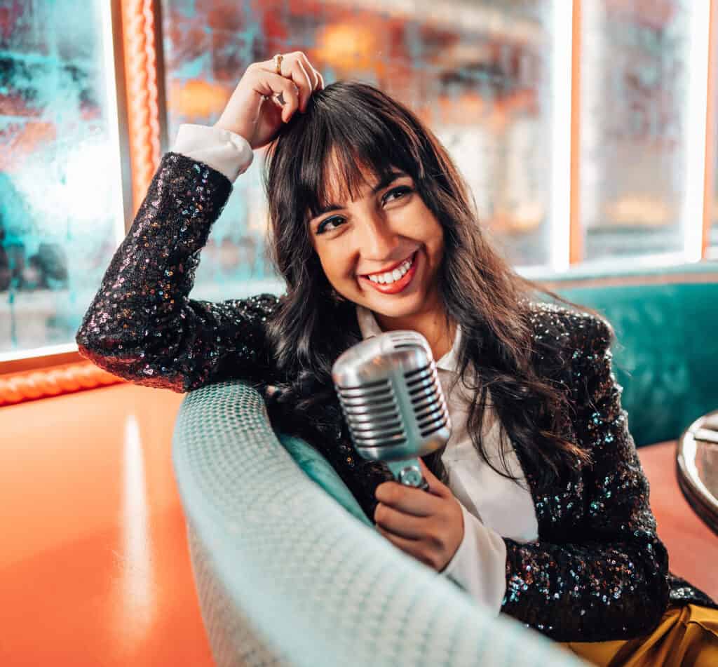 Lissette Calviero smiling while sitting in a diner booth with a microphone.